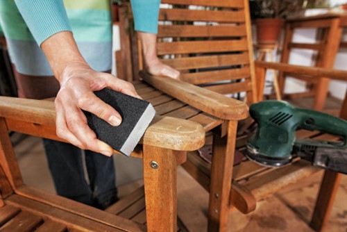 Lady maintaining a loveseat by sanding it down getting it ready to paint with oil