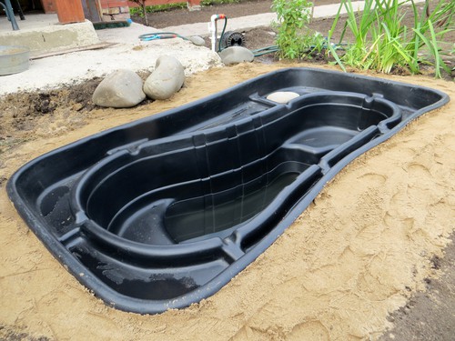 Testing of an installed preformed plastic pond insert filled with some water in the summer garden