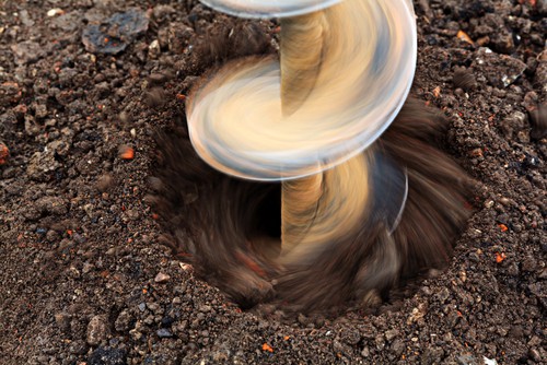 Earth auger being used on gritty soil to dog holes