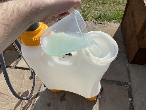 Pouring the dissolved iron sulphate into garden sprayer before topping up with cold water 