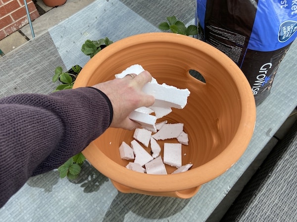 Adding crockery to the bottom of a strawberry planter to prevent the hole becoming clogged up