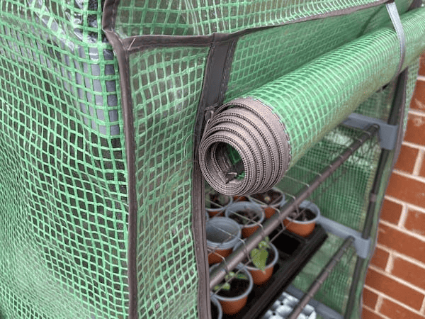 The door on the Woodside 4 Tier Garden Greenhouse rolls up